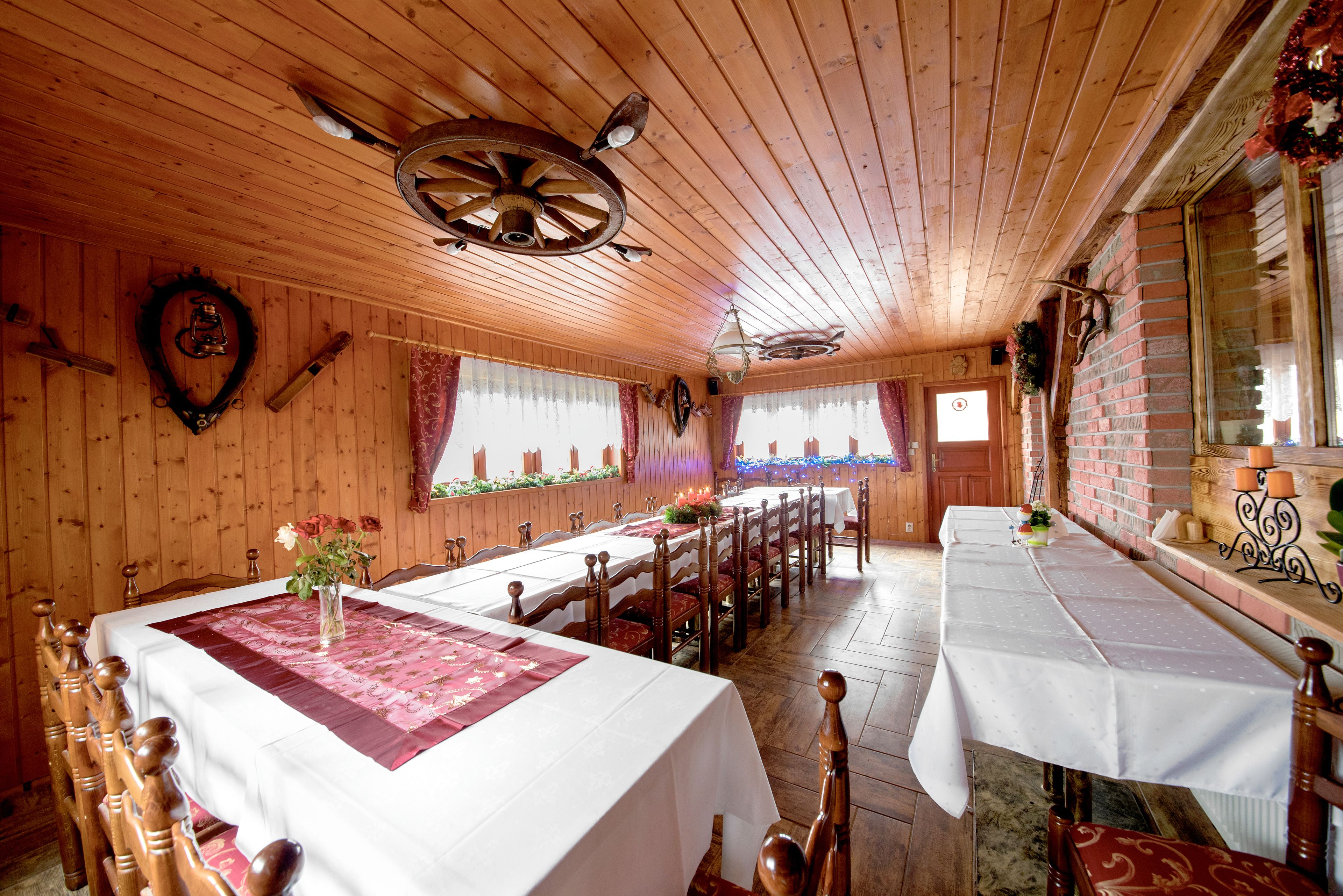 A wooden interior with a long dining table, multiple chairs, and a chandelier.