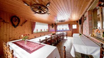 A wooden interior with a long dining table, multiple chairs, and a chandelier.