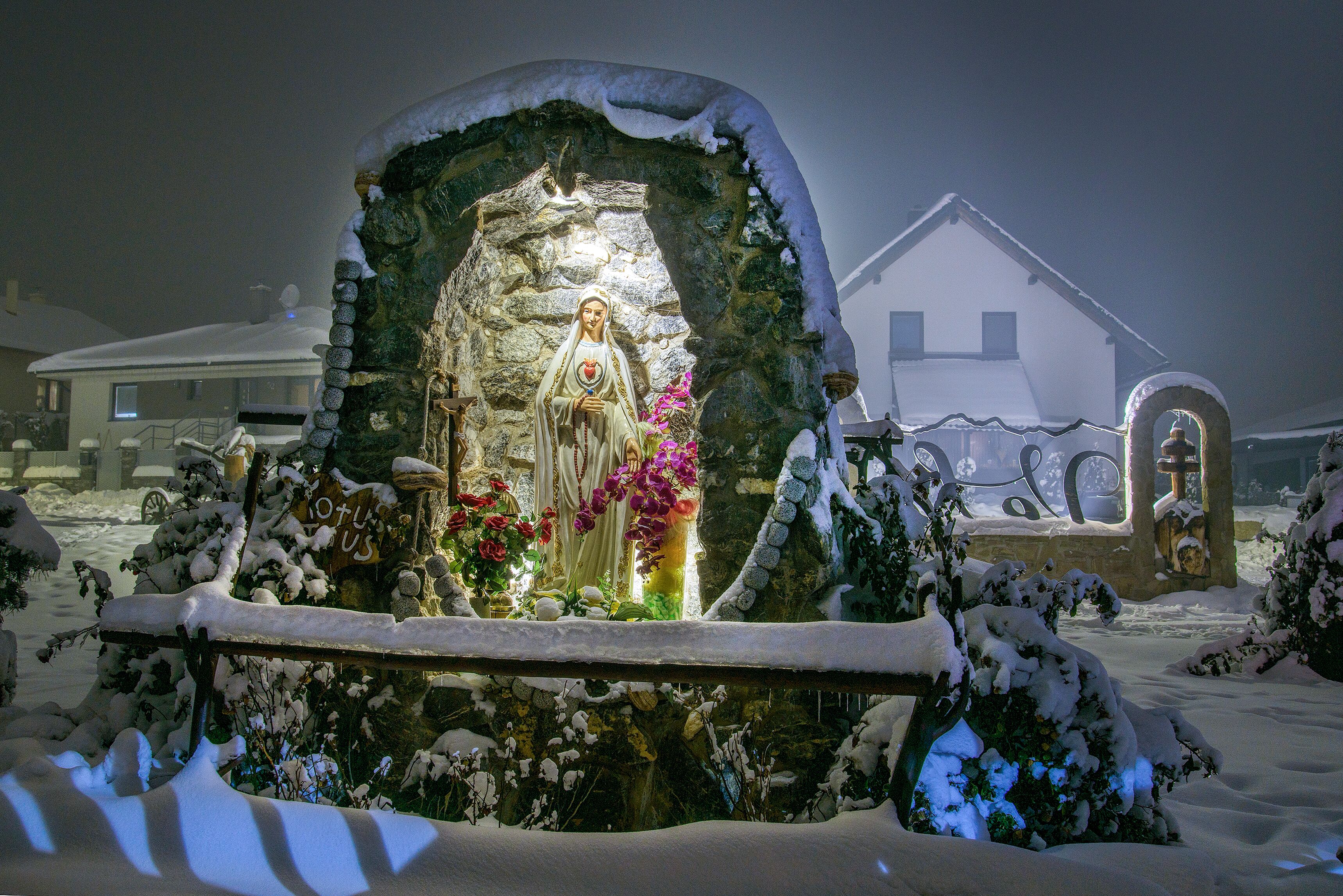 Un espacio exterior cubierto de nieve con una estatua, un arco de piedra y una casa al fondo.