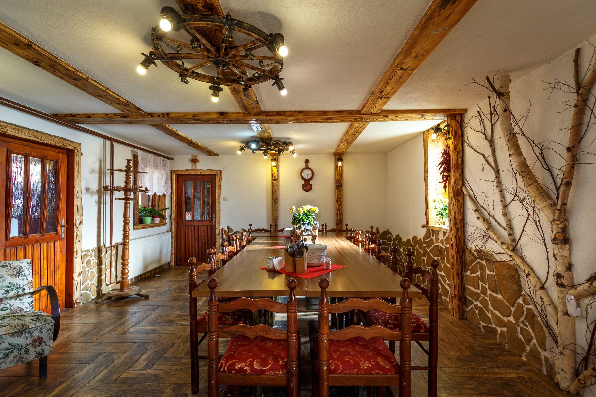 A dining room with a long wooden table, wooden chairs, a chandelier, and a stone wall.