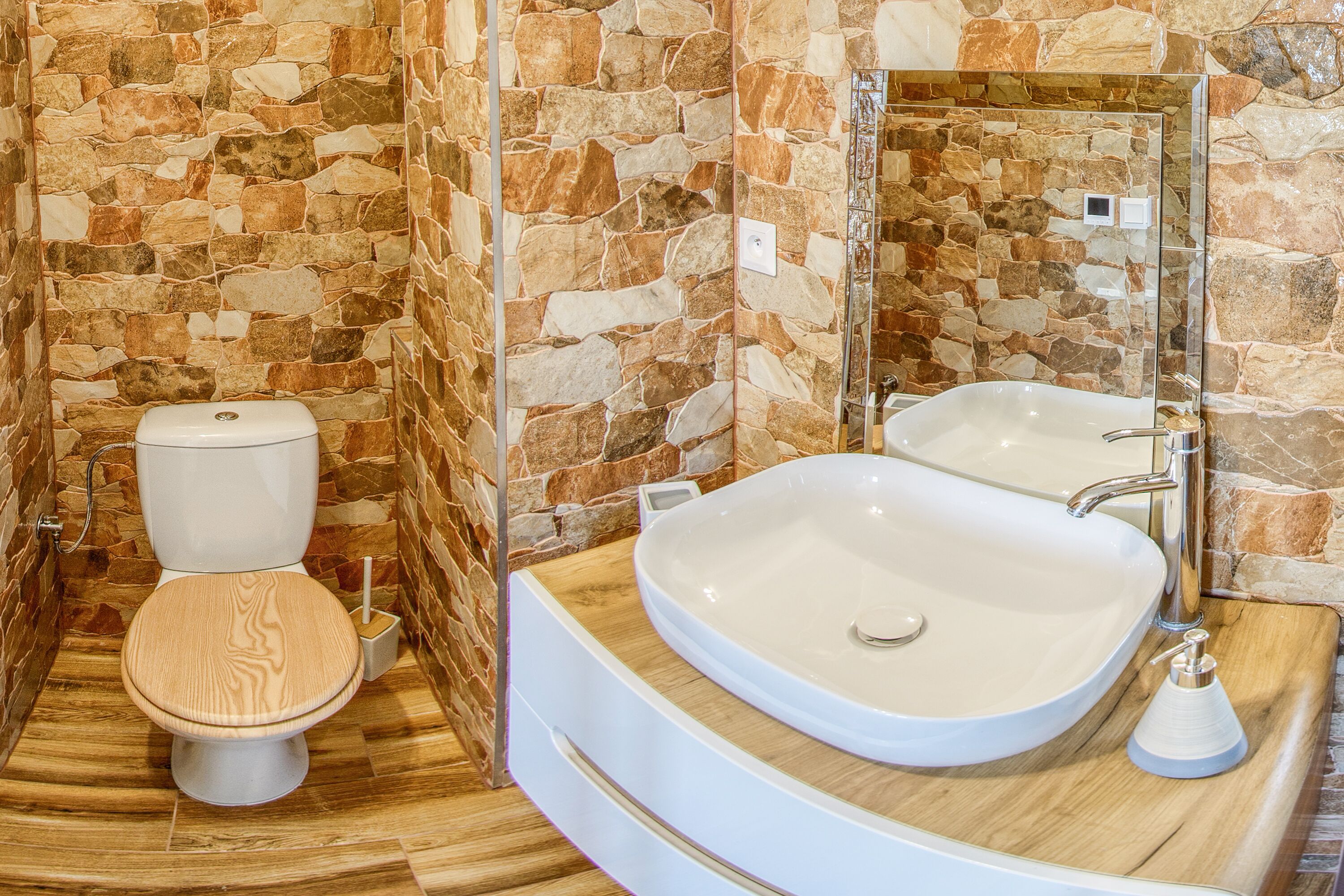 Une salle de bain avec un mur en pierre, des toilettes blanches et un grand lavabo blanc avec un miroir au-dessus.