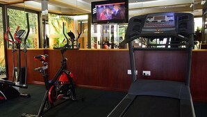 A gym with a treadmill, stationary bikes, and a TV screen displaying a program. - Pinnacle Court Apartments (Nairobi)