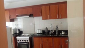 A kitchen with wooden cabinets, a stove, a refrigerator, and a countertop with kitchen utensils. - Pinnacle Court Apartments (Nairobi)