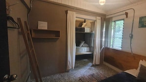 Et lille værelse med køjeseng, et vindue med gardiner, en træsenggavl og en reol monteret på væggen.