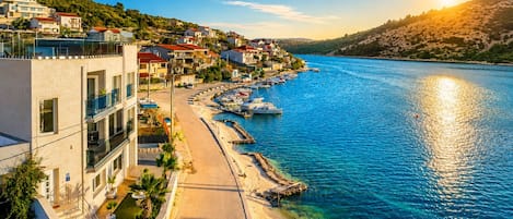 A coastal town with buildings along a waterfront, a clear sky, and boats docked near the shore.