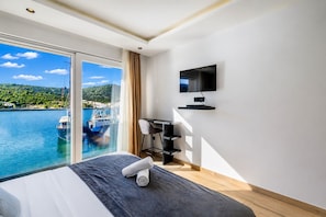Une chambre d’hôtel équipée d’un lit, d’un bureau, d’une télévision et d’une grande fenêtre donnant sur les bateaux et l’eau.