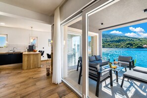 A modern kitchen with a wooden island, a dining area with a table and chairs, and a balcony with a view of the sea.