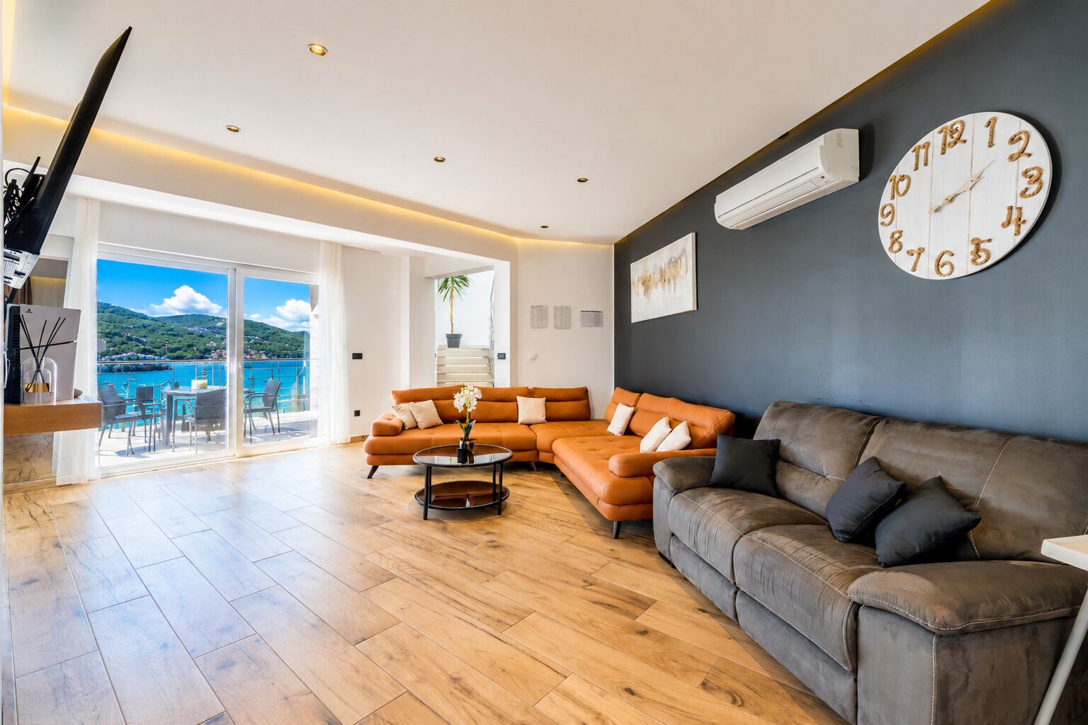 Un salon spacieux avec un grand canapé, une table basse et une vue sur la mer grâce à de grandes portes vitrées.
