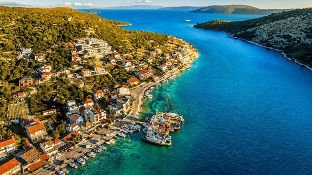 An aerial view of a coastal town with buildings along the waterfront, boats docked at the pier, and a clear blue sea. - Beachront Luxury Villa w/rooftop pool, gym + spa Only 20 Min. From Split Airport (Vinišce)