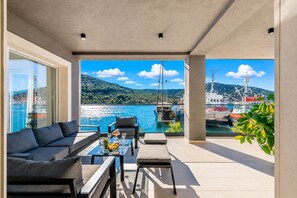 Un espace extérieur moderne aménagé avec des sièges, offrant une vue sur un port de plaisance et des collines.