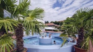 A circular hot tub surrounded by palm trees and a pool area. - Apparthotel Jagdhof (Bad Griesbach im Rottal)