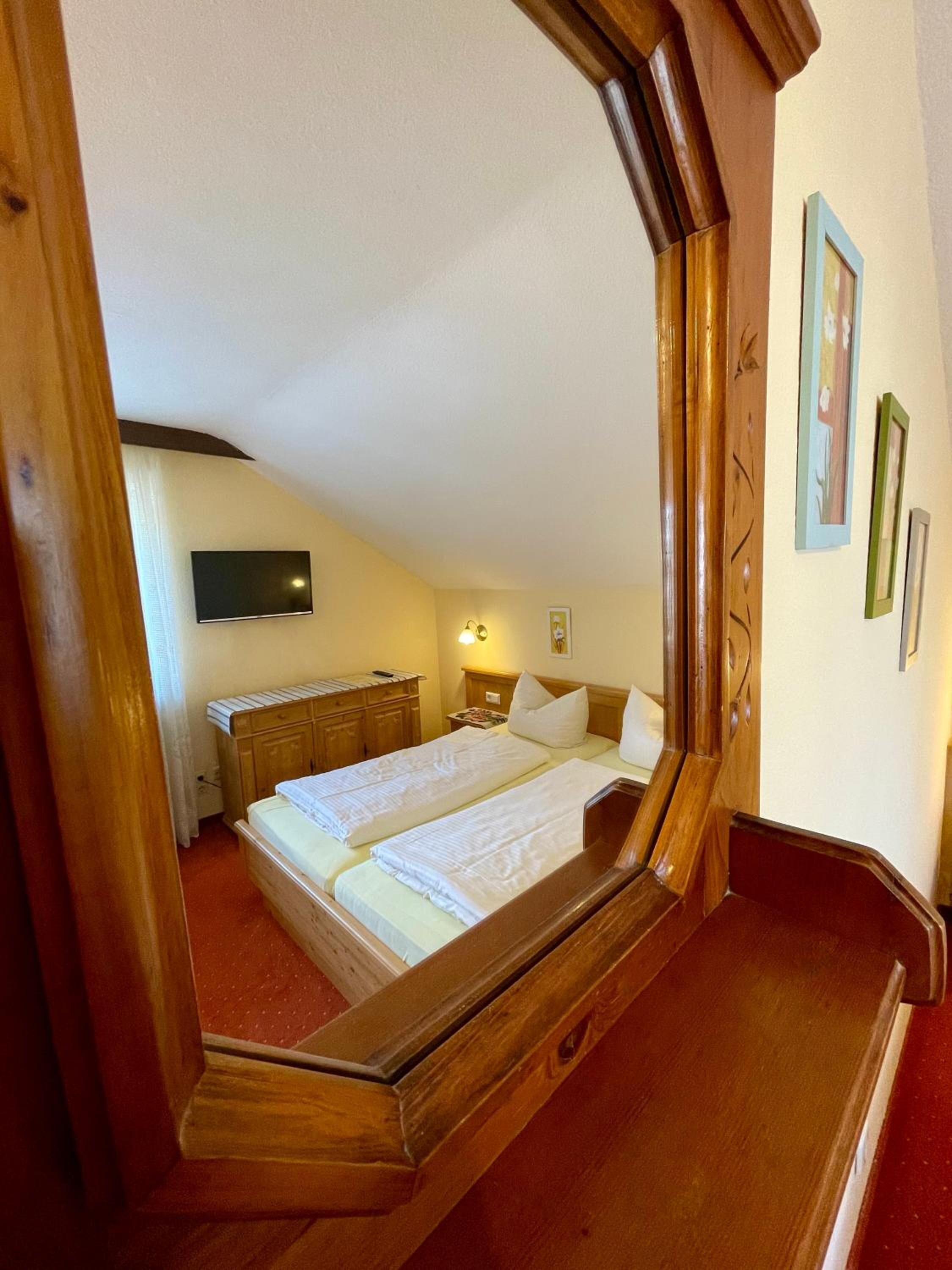 A bedroom with a wooden bed frame, a flat-screen TV mounted on the wall, and a bedside table with a lamp.