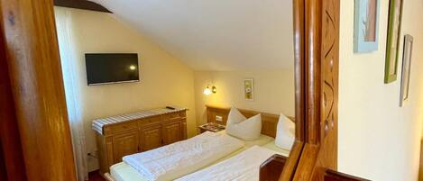 A bedroom with a wooden bed frame, a flat-screen TV mounted on the wall, and a bedside table with a lamp.