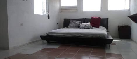 A bedroom with a bed, a window, and a trash bin.