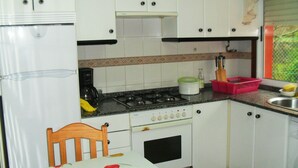 Una cocina compacta con armarios blancos, estufa y pileta.