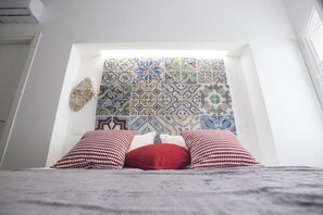A bedroom with a patterned tile wall, a bed with checkered and solid pillows, and a stone accent piece. - Real Fonderia b&b (Palermo)