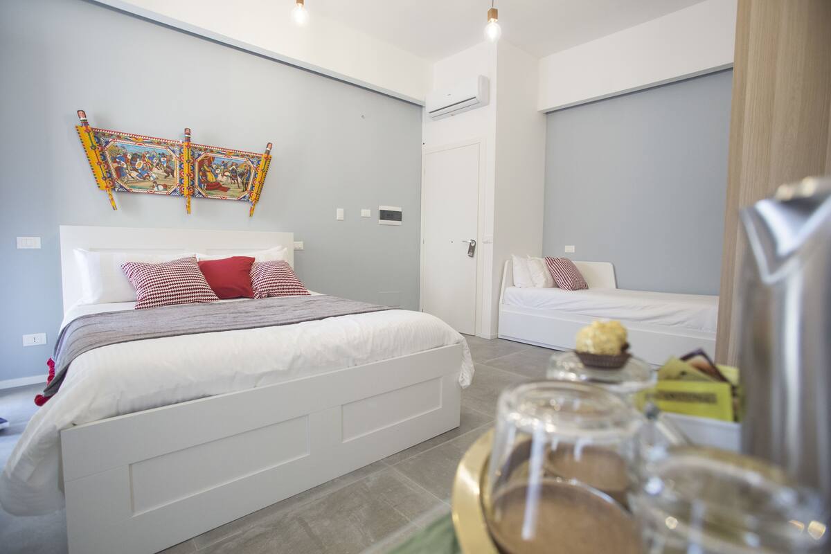 A modern hotel room with a large bed, a smaller bed, and a dining table with food and drinks.