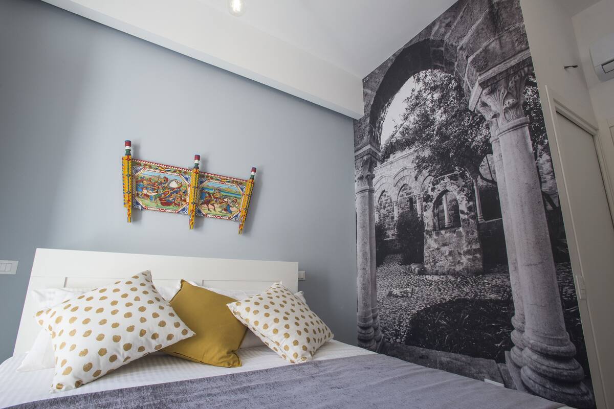 A bedroom with a bed, pillows, a wall tapestry, and a large mural.