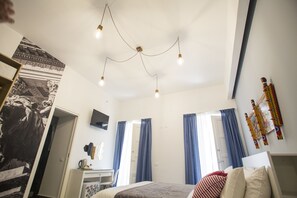 A bedroom with a bed, a desk, a chair, a television, and a large tapestry on the wall. - Real Fonderia b&b (Palermo)