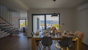 Uma área de refeições moderna com mesa de vidro, cadeiras e vista para o exterior.