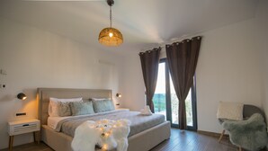 Quarto com cama, mesas de cabeceira, luminária pendente, uma cadeira e vista pela janela.