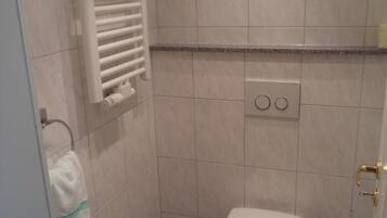 Une petite salle de bain carrelée, équipée de toilettes, d’un porte-serviettes et d’un radiateur.