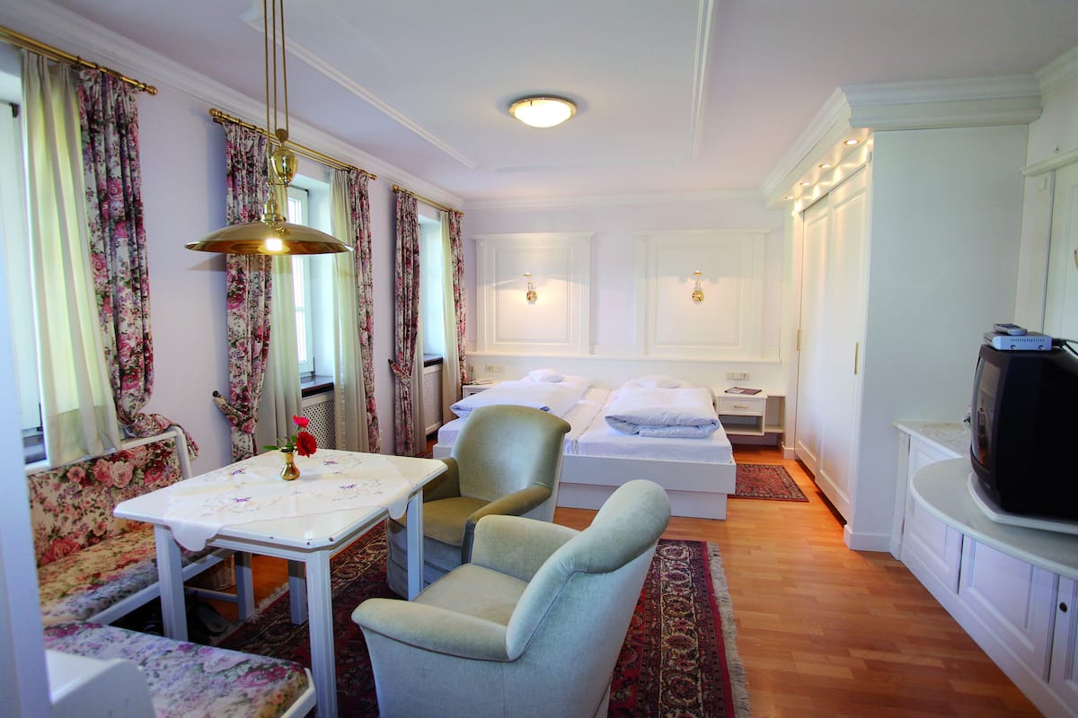 Quarto de hotel com cama, televisão, mesa com cadeira, sofá e cortinas.