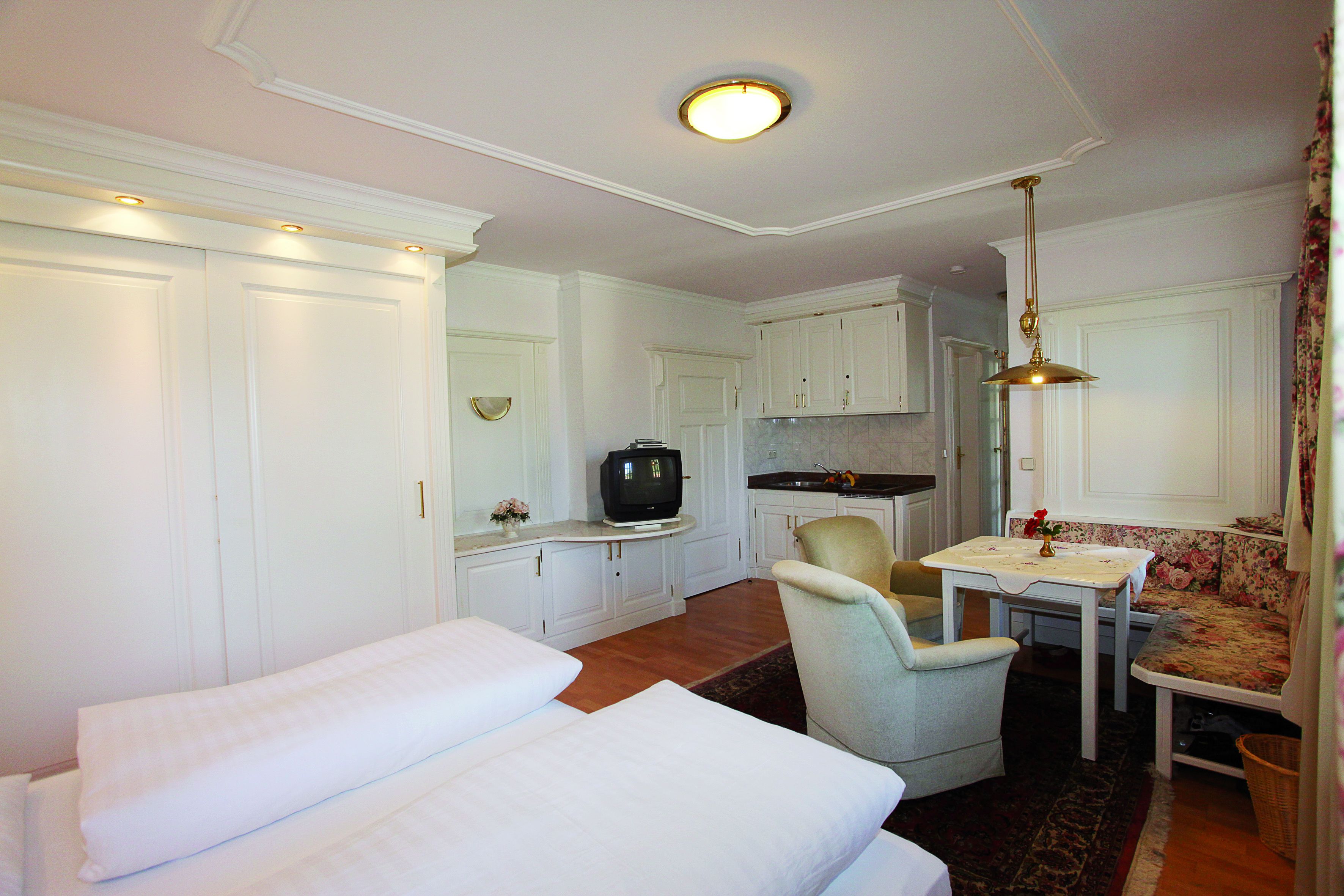 A compact, well-lit room with a bed, a small dining table, a chair, and a television.