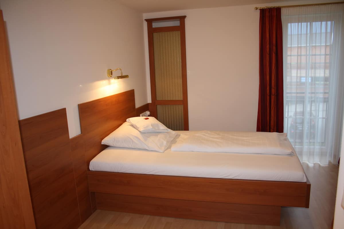 Uma cama de solteiro com cabeceira de madeira, roupa de cama branca e mesa de cabeceira com abajur.