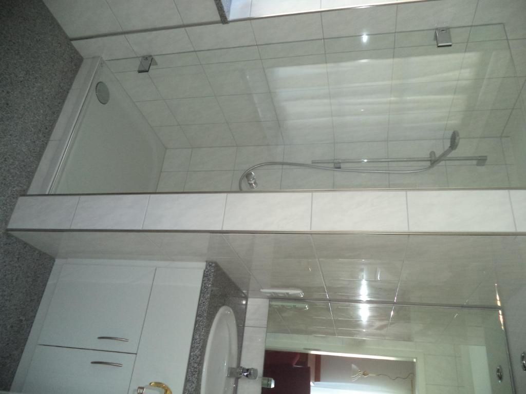 Un baño con cabina de ducha de vidrio, un lavabo blanco y un mueble con cajones.