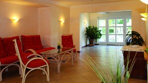 A room with a red sofa, white chairs, a small table, and a potted plant.