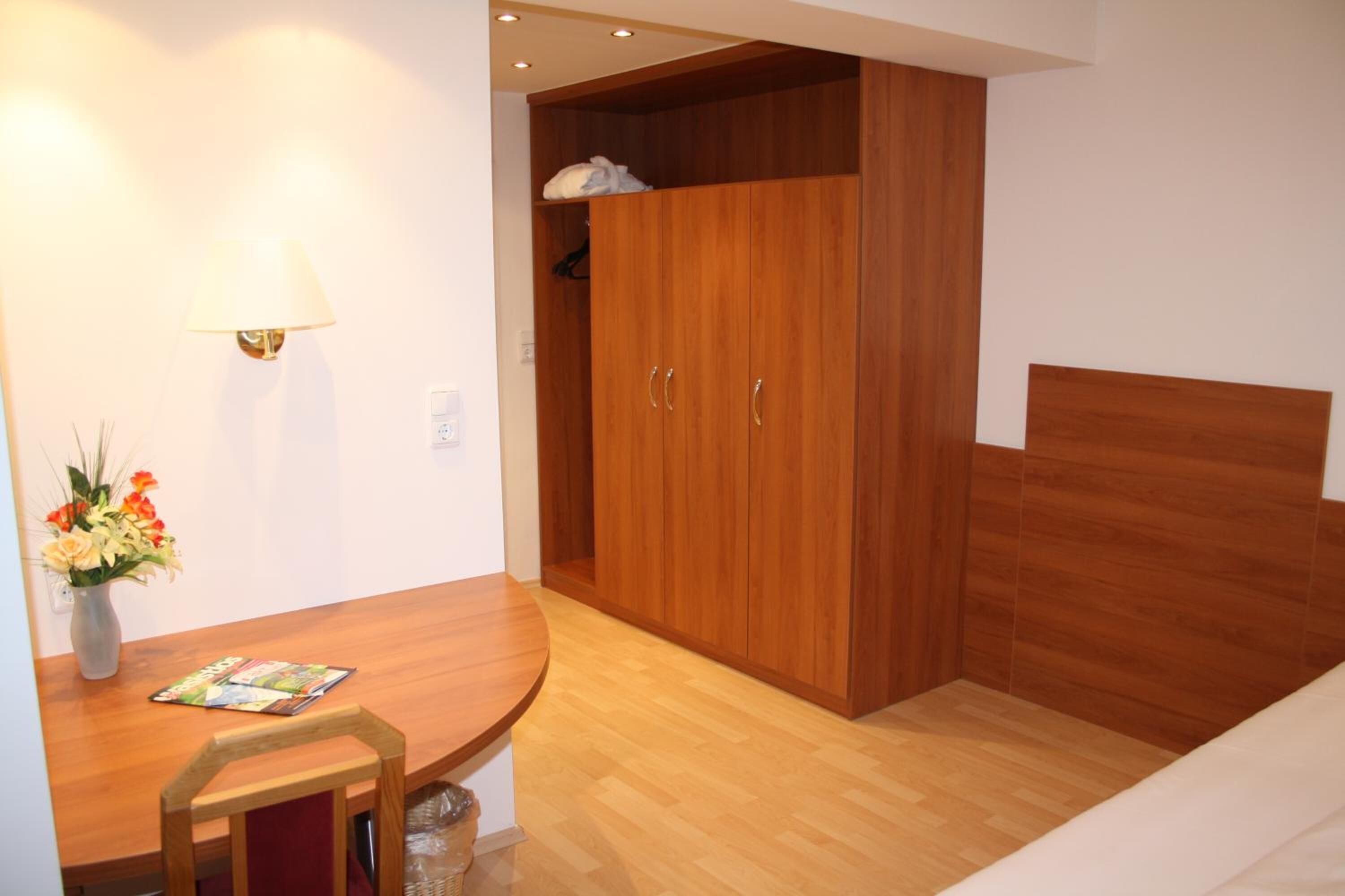A room with a wooden dining table, a chair, a lamp, and a wardrobe.