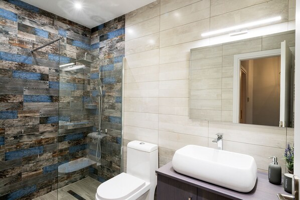 A bathroom with a glass shower enclosure, a white toilet, and a vanity with a large sink.