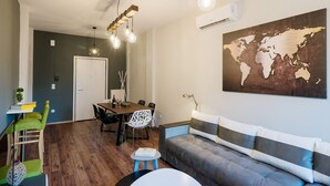 A modern living room with a grey sofa, a dining table with chairs, a wooden floor, and a world map on the wall.