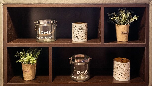 A modern living room with a wooden console table, decorative jars labeled "Home Sweet Home," and a potted rosemary plant.