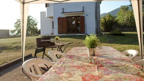 An outdoor dining area with a table set for two, a potted plant, and a view of a modern house with a patio.