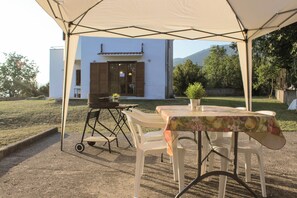 Ein Essbereich im Freien mit Tisch und Stühlen unter einem Zelt, ein kleiner Tisch mit einer Pflanze und ein Gebäude im Hintergrund.