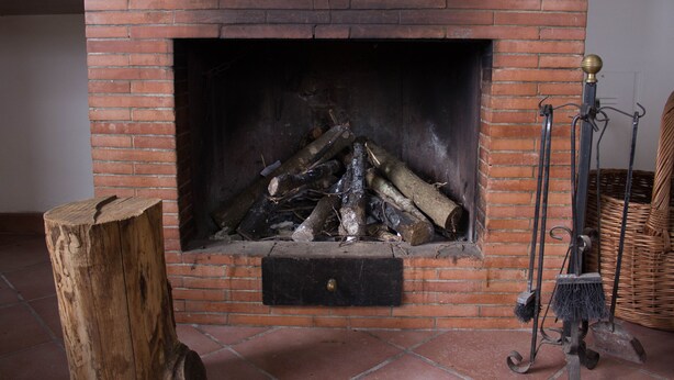 A brick fireplace with logs, a wooden stump, and a broom.