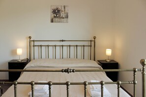 Ein ordentlich bezogenes Bett mit Metallgestell, zwei Nachttische mit Lampen und ein Wandbild.