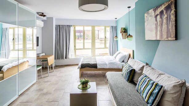 A modern bedroom with a bed, a sofa, a desk, and a large window. - Emerald Suite (Athens)