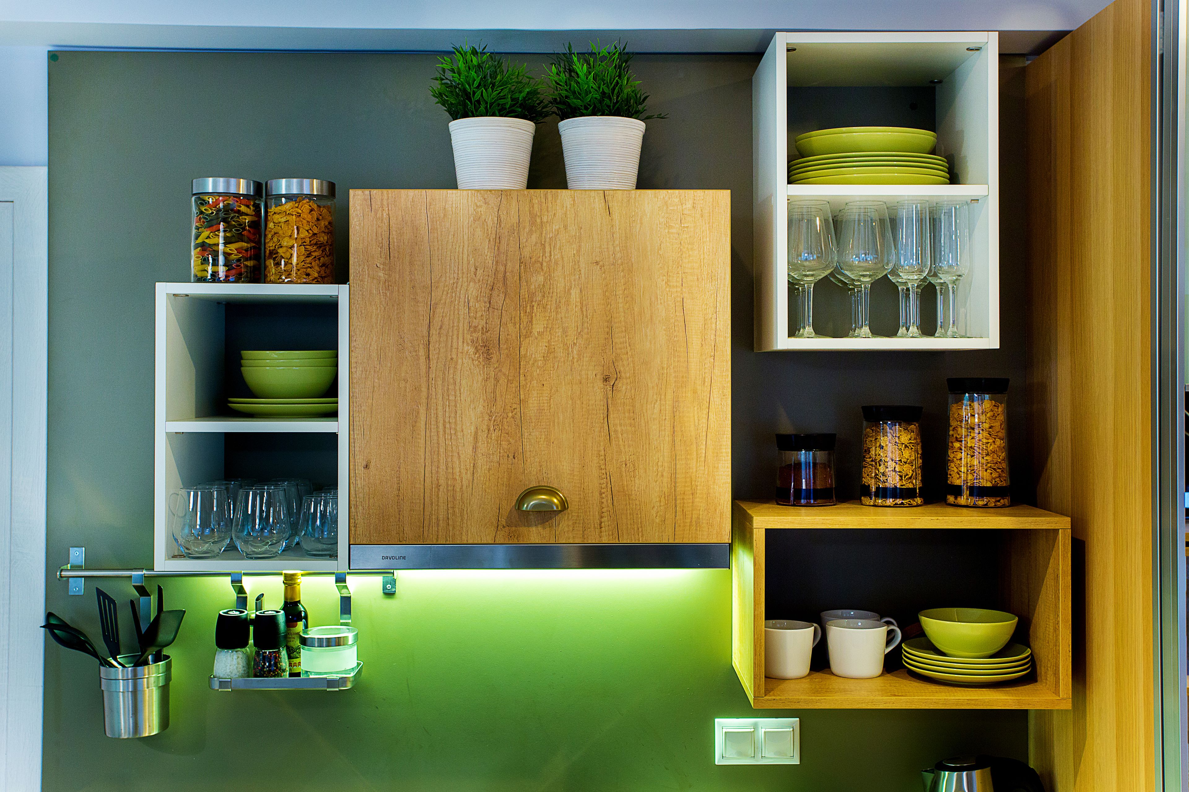Une cuisine avec des meubles en bois, des plans de travail verts et divers ustensiles de cuisine, notamment des bols, des tasses et des verres à vin.