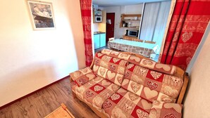 A cozy room with a patterned sofa, a wooden floor, and a kitchen area visible through an open door.