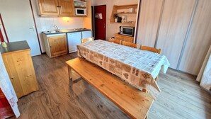 A compact kitchen with wooden cabinets, a microwave, and a toaster. There's a dining table with a patterned tablecloth and a bench.