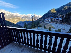 A balcony with a view of a mountain range, a parking area, and buildings with red roofs. - Valfréjus Apt 6/8 pax, 2 BAs, Balcony, Central Location (Valfréjus)