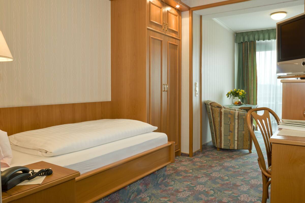 A hotel room with a bed, a desk, a chair, a telephone, and a television.