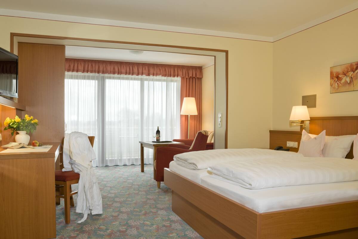 A hotel room with a bed, a desk, a chair, a lamp, and a window with curtains.
