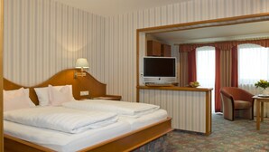 Habitación de hotel con una cama grande, un televisor sobre un mueble, un escritorio con una silla y vistas a través de una puerta abierta.