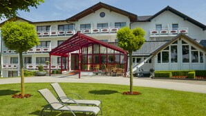 Un hotel con una zona de estar exterior cubierta, piscina y césped bien cuidado.