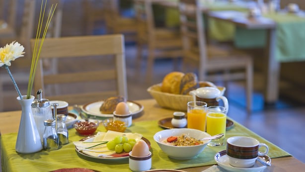 Una mesa de desayuno con platos de comida, un jarrón con flores y una taza de café.