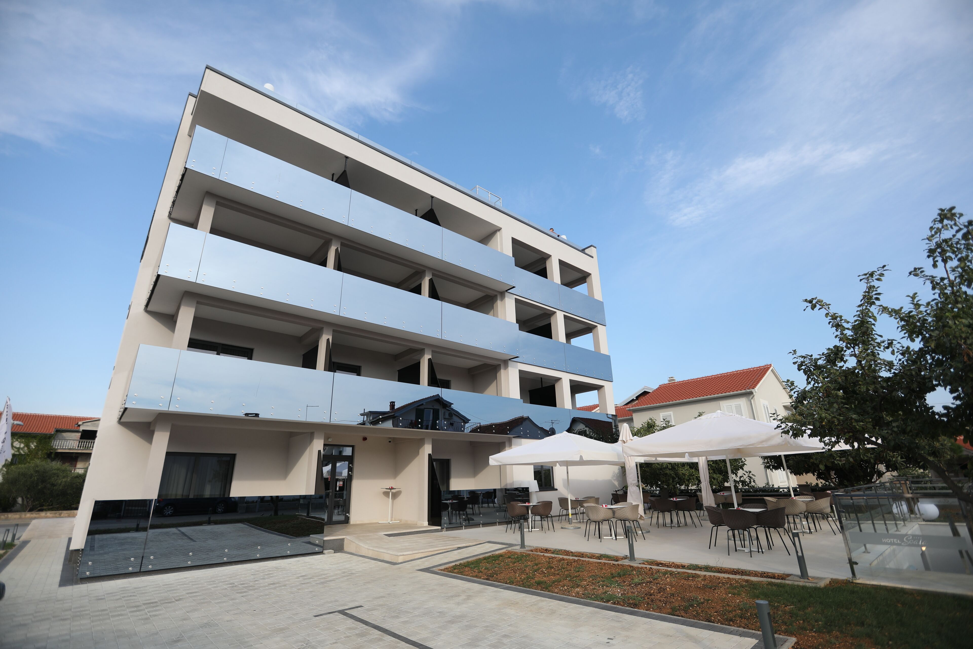 A multi-story hotel with a flat facade, outdoor seating area, and a clear sky.